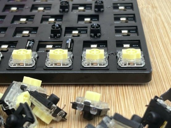 A close-up image of a mechanical keyboard build in progress, showing partially installed yellow mechanical switches, with several switches lying scattered in the foreground.