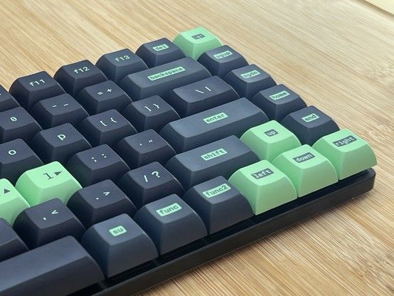 Close-up of a mechanical keyboard with black and green keycaps on a wooden surface.