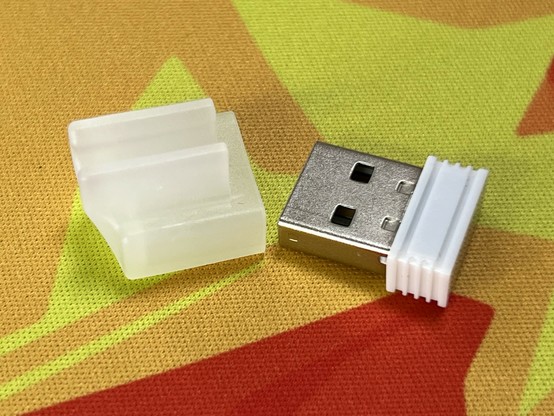 A USB wireless dongle and a transluscent white storage cap on a colorful fabric surface.