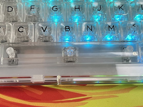 Close-up of a mechanical keyboard with transparent keys and blue backlighting. The space bar is transparent too, showing the stabilizers and single lone LED underneath.
