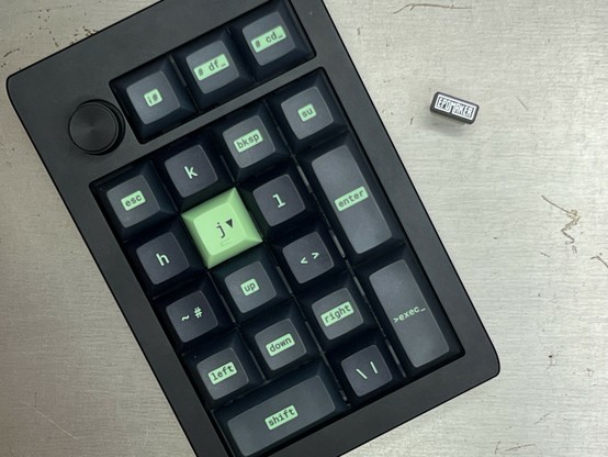 A top down photo of a mechanical keyboard macro pad with green keycaps suggesting it functions as a VIM navigation aid with a mix of random Linux commands and special characters on other keys.