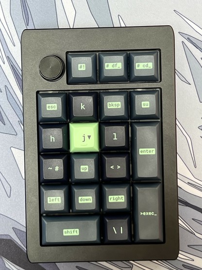 A compact mechanical keyboard with various key labels, including navigation keys and programming shortcuts, and a large knob on the top left corner.