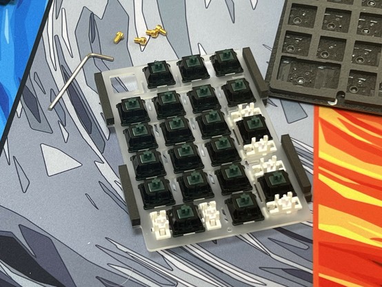 A partially assembled mechanical keyboard macro pad with dark green switches, a hex key, small screws, and a keyboard PCB off to one side.