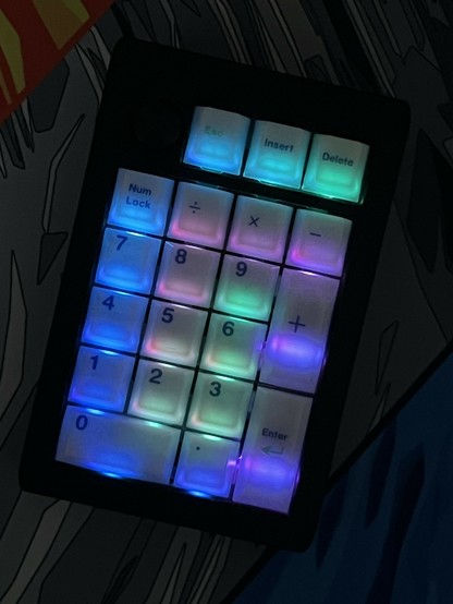 A numeric keypad with glowing, translucent, multicolored backlit keys on a patterned background.