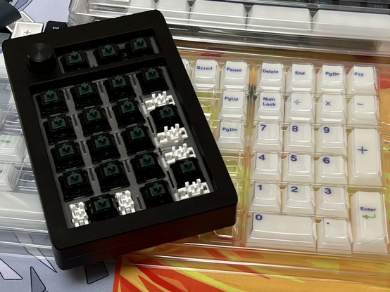 A mechanical keyboard numpad with dark green switches installed sitting atop a tray of white translucent keycaps with numeric and functional keys.