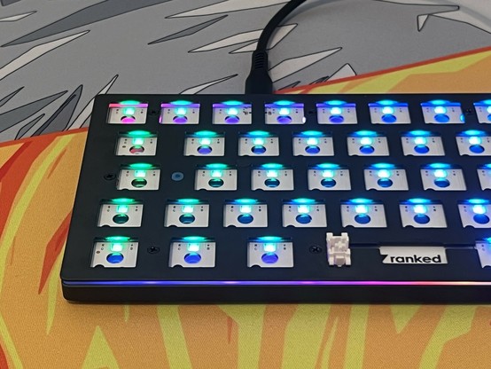 A mechanical keyboard without keycaps or switches, showcasing illuminated RGB backlighting, placed on a colorful desk mat.
