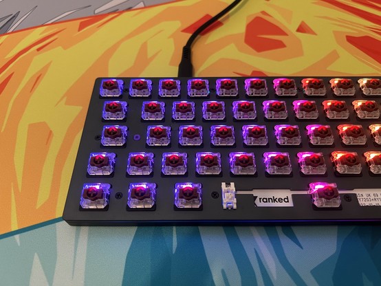 RGB mechanical keyboard with the caps off revealing colourful backlight switches set on a colorful desk mat with a bold, abstract design.