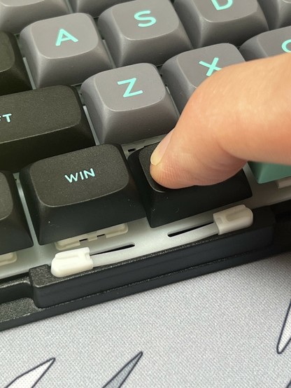 A hand pressing a key on a mechanical keyboard. The top case has been removed showing the mount for the keyboard plate flexing under the pressure.