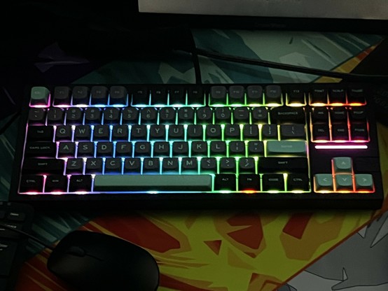 A mechanical keyboard with RGB backlighting displaying multiple colors. A computer mouse is partially visible below the keyboard.