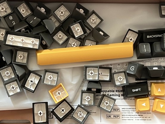 Scattered keyboard keycaps, including yellow, black, and gray ones, display labels like 