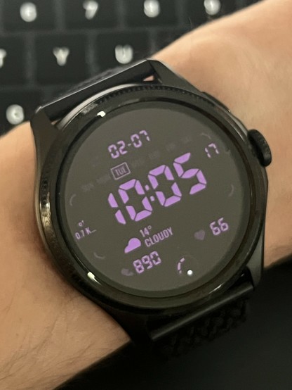 The smartwatch OLED display turned on showing purple digits on a black background, matching but inverting the low power display.