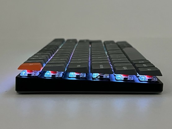 A low angle side view of a low-profile mechanical keyboard with RGB backlighting and an orange escape key.