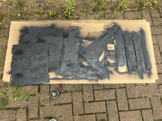 Spray-painted black wooden panels laid out on a piece of cardboard on a brick paved surface.