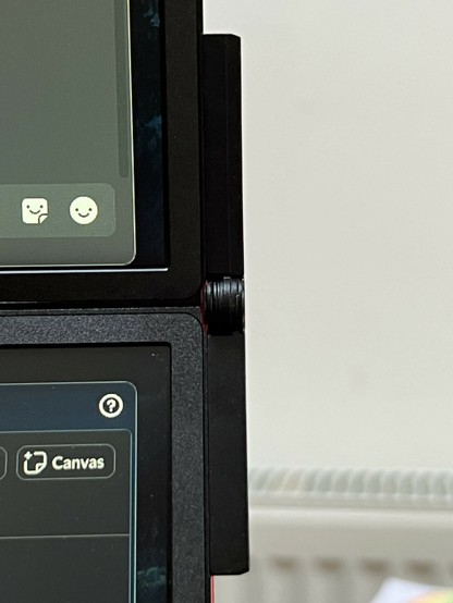 An image showing the edge and hinge of two stacked computer monitors, with a part of the screen visible displaying icons and user interface elements.