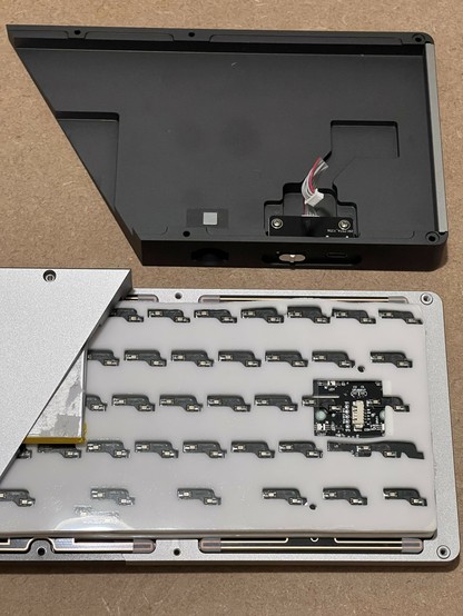 An interview view of the KiiBOOM Loop 65 showing one half of the bottom removed and revealing some damping material, key switch sockets, and some PCB and a battery peeking out. 