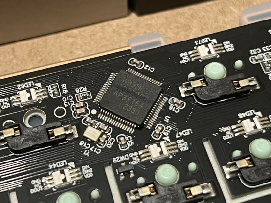 Close-up of a circuit board featuring various electronic components, including a microchip, capacitors, and switches. The board is predominantly black with white printed labels and circuit traces. The focus is on a chip marked WB32F, if that sounds suspiciously like STM32F then your instincts are sound.