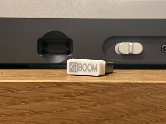 A USB dongle removed from the back of a keyboard and set aside on a wooden surface. It’s labelled KiiBOOM.