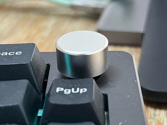 A close up of a smooth silver flat topped knob on a mechanical keyboard.