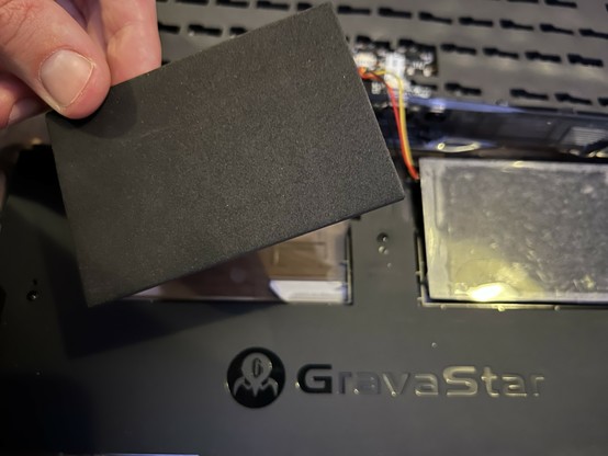 A hand holding a piece of black blanking foam over its recess in the bottom of a mechanical keyboard.