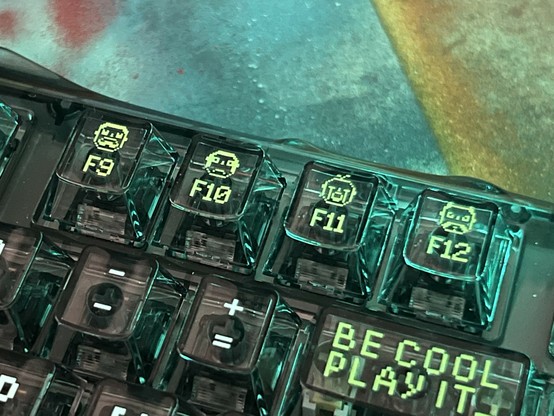 A close-up view of a gaming keyboard featuring function keys F9 to F12, each adorned with unique pixel art faces. The keyboard has a translucent, black design and the backspace key is labelled 