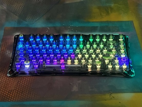 A brightly lit mechanical keyboard featuring multicolored backlit keys in shades of blue, purple, and green, set against a textured background.