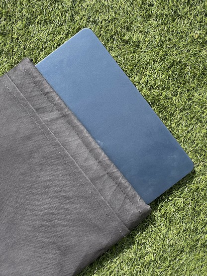 A dark blue laptop partially covered by a gray sleeve resting on green artificial grass.