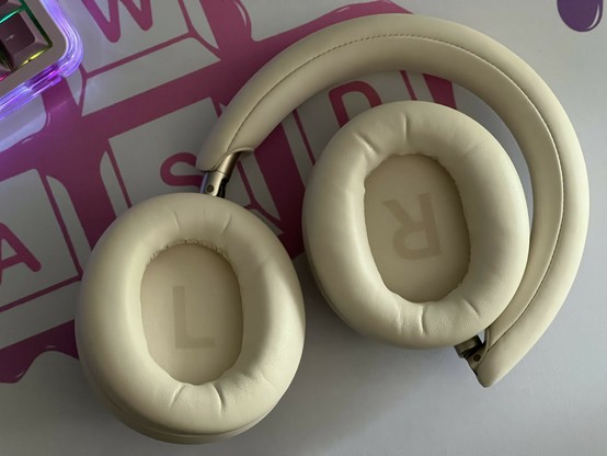 A pair of chunky white over ear headphones playing on a white desk mat with the ear cups facing upwards. L and R lettering is visible inside them.