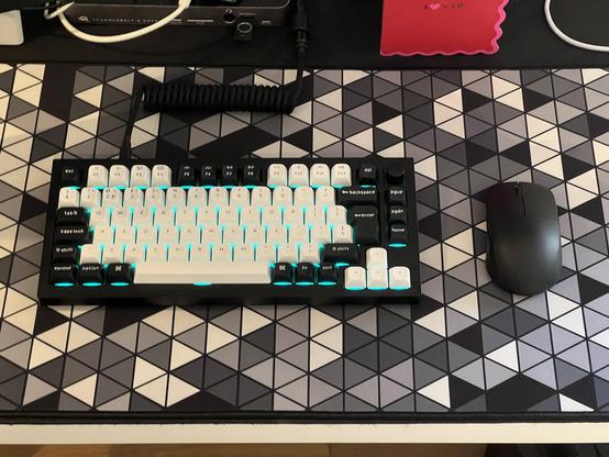 A compact black keyboard with contrasting black and white keycaps sat atop a greyscale deskmat with a geometric pattern of teslating triangles.