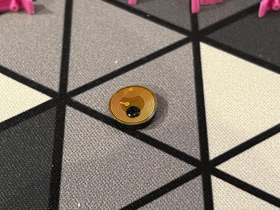 A tiny flex PCB with a trace forming the concentric circles of a spiral antenna. Offset from the middle is a tiny dot of shiny black potting compound.