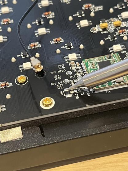 The empty SMA connector pads on the PCB being soaked by a hot soldering iron in preparation for soldering. The broken off connector and cable sit sadly nearby.