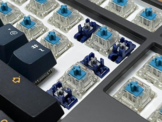 A close up of a mechanical keyboard with the enter key and surrounding caps removed. Underneath are blue and clear switches.