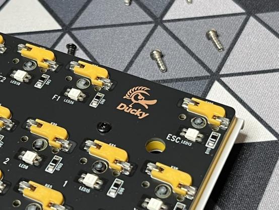 A close up of the corner of the Ducky keyboard PCB. There's a small Ducky logo, surrounded by bright yellow switch sockets which match the yellow damping material just visible on the reverse.