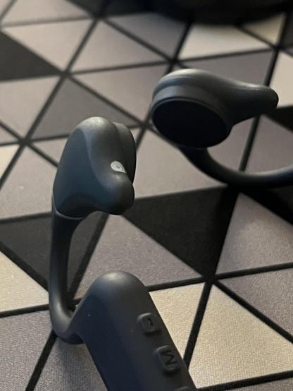 A close up of a pair of bone conduction headphones on a geometric grey deskmat.