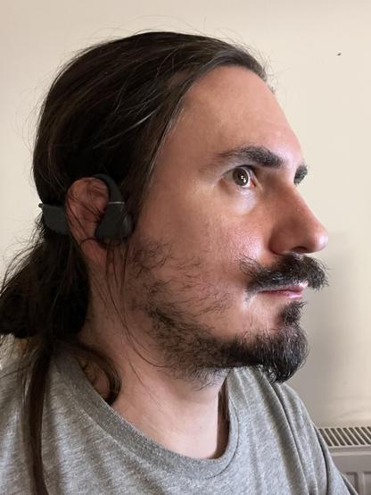 A photo of me, a man with long hair, a moustache, and a threatening-to-be-a-neckbeard wearing some just visible headphones on what - under close inspection - looks like the ear of a professional rugby player.