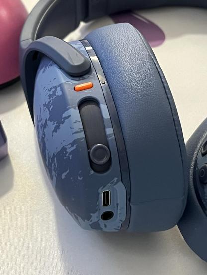 The left ear up of some blue headphones, a large slider dominates most of the back beneath a tiny orange power button.