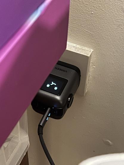 A slightly bent USB C cable coming out of a wall adapter. The adaptor has a little monochrome face snapshotted in the middle of its chewing/charging animation cycle.