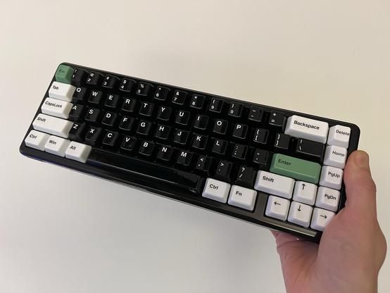 A person holding a black and white mechanical keyboard featuring glossy ceramic keycaps. The keyboard has a compact 65% layout without function keys.