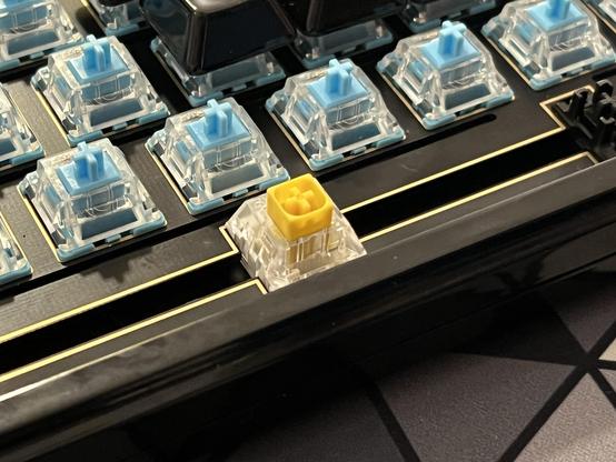 Closeup of the space bar switch on a mechanical keyboard. It’s yellow and of a slightly different design to the blue of the other switches.