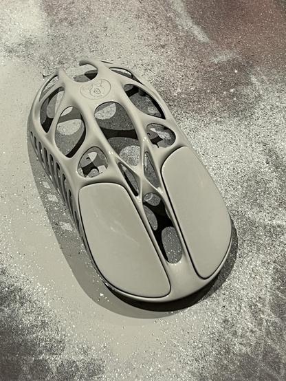 A metal outer shell of a gaming mouse painted white, sat on a sheet of spray splattered cardboard.