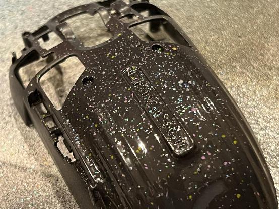 The inner plastic shell of a gaming mouse painted black with glitter sprinkled into the paint.