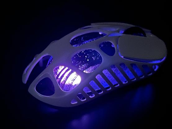 A white skeletal gaming mouse with a black inner shell glowing purple.