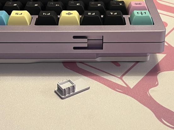 A small plastic clip sat in front of the back edge of a mechanical keyboard where it’s supposed to secure the top and bottom half together.