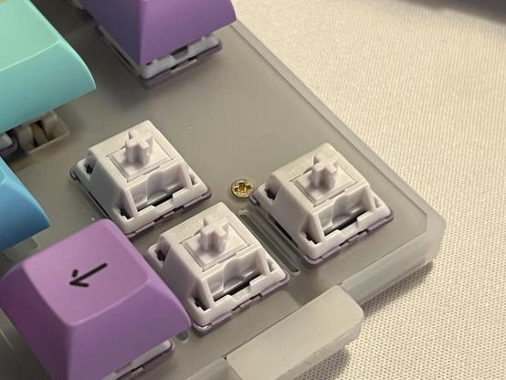 A closeup of an off white plastic mechanical keyboard plate with a single brass screw nestled between the arrow key switches.