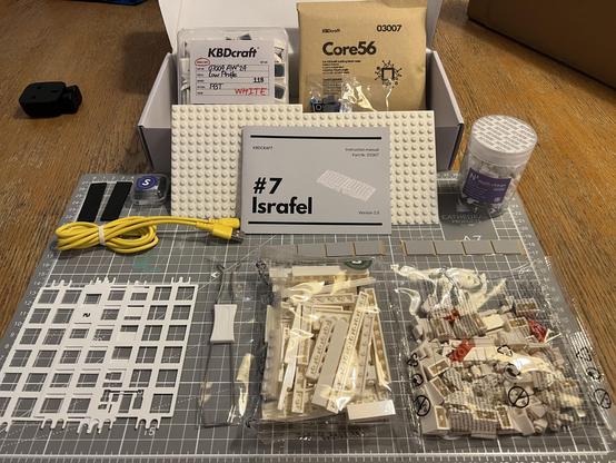 An open Israfel keyboard kit with bags of LEGO-style pieces laid out in front alongside more traditional mechanical keyboard parts.