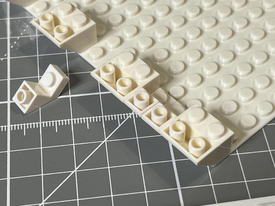 Inverted LEGO-style brick slopes being assembled onto a base plate. Sole are the standard two studs wide, but others are one stud with a little recess. This will be relevant later.