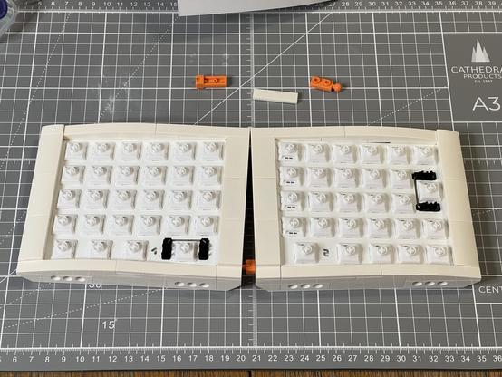 A completed LEGO-style brick split keyboard waiting for keycaps. Some orange hinge bricks and a flat 1x4 white plate sit above.