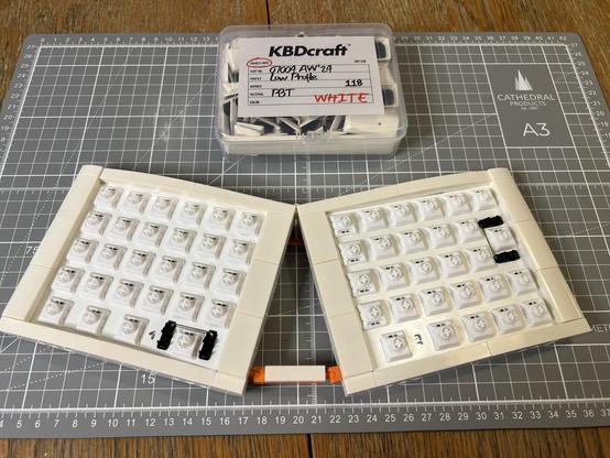 The completed split keyboard with a box of 118 white low profile PBT keycaps sat above.