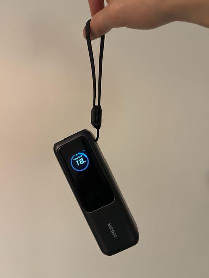 A portable battery hanging from its lanyard, which doubles as a captive USB C charging cable.