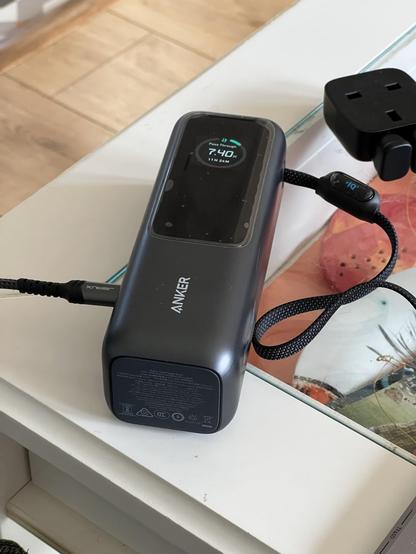 A portable battery sat on a table with wires trailing off in two directions. The words “Pass Through” are just visible on screen with an 11 hour recharge estimate.