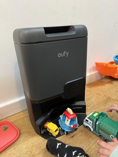 The base station for a robot vacuum cleaner with various toy cars and trucks parked in the bottom.